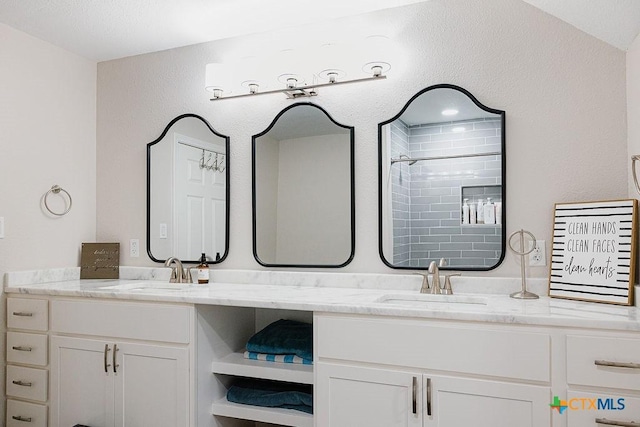 full bath featuring double vanity, a sink, and tiled shower