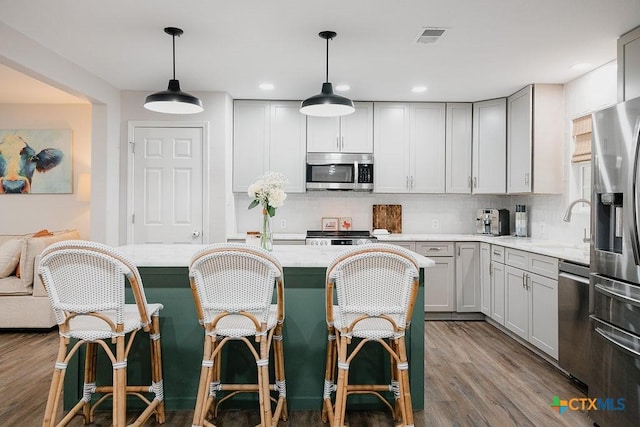 kitchen featuring tasteful backsplash, visible vents, appliances with stainless steel finishes, light stone counters, and hanging light fixtures