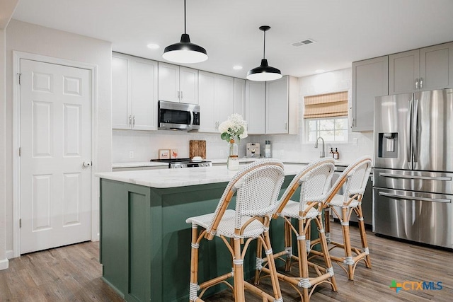 kitchen featuring light stone counters, decorative light fixtures, stainless steel appliances, visible vents, and a kitchen island