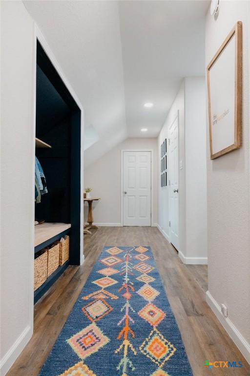 corridor featuring dark wood-style floors, lofted ceiling, and baseboards