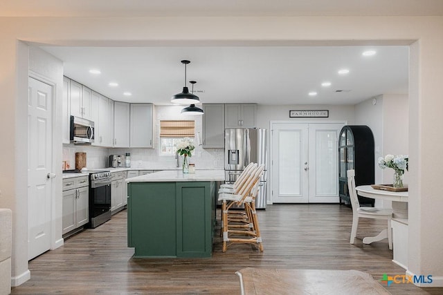 kitchen featuring stainless steel appliances, hanging light fixtures, light countertops, a center island, and a kitchen bar