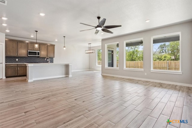 unfurnished living room featuring ceiling fan with notable chandelier, light hardwood / wood-style floors, and sink