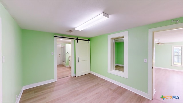 spare room with a barn door, ceiling fan, and light hardwood / wood-style flooring