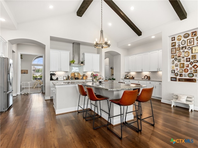 4508 River Rock Rd, Marion, TX 78124 - kitchen with stainless steel fridge, wall chimney exhaust hood, arched walkways, beamed ceiling, and a center island with sink