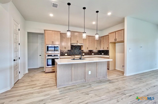 kitchen featuring appliances with stainless steel finishes, decorative light fixtures, a kitchen island with sink, and light brown cabinetry