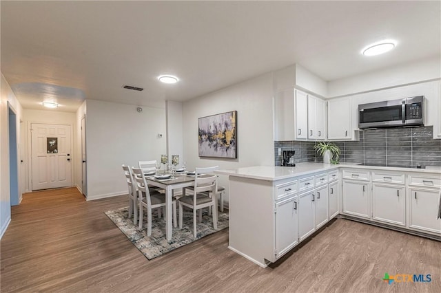 kitchen with white cabinets, decorative backsplash, hardwood / wood-style flooring, kitchen peninsula, and black electric cooktop