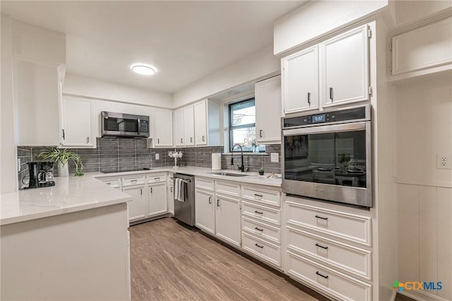 kitchen featuring sink, stainless steel appliances, tasteful backsplash, white cabinets, and light wood-type flooring