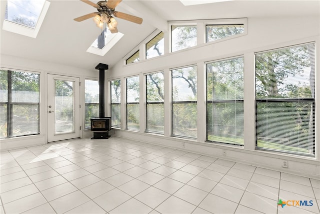 unfurnished sunroom with a wood stove, ceiling fan, and vaulted ceiling with skylight