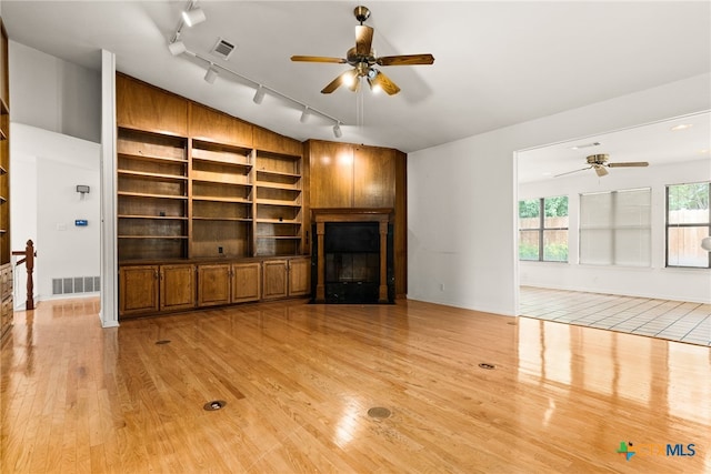 unfurnished living room with a fireplace, rail lighting, light hardwood / wood-style flooring, and ceiling fan