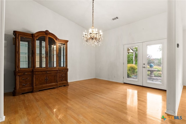 unfurnished dining area with a chandelier, light wood-type flooring, and french doors