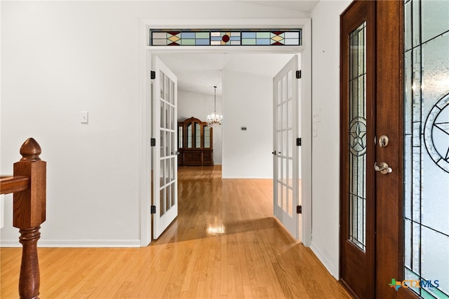 hall with lofted ceiling, wood-type flooring, a chandelier, and french doors