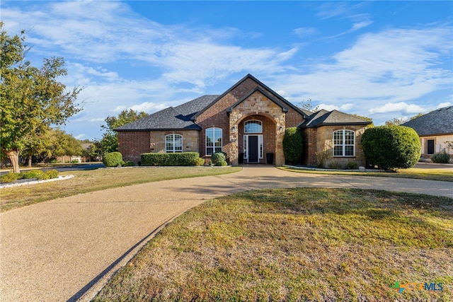 french country inspired facade featuring driveway, stone siding, and a front yard