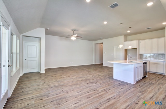 kitchen with hanging light fixtures, a kitchen island with sink, white cabinets, sink, and backsplash