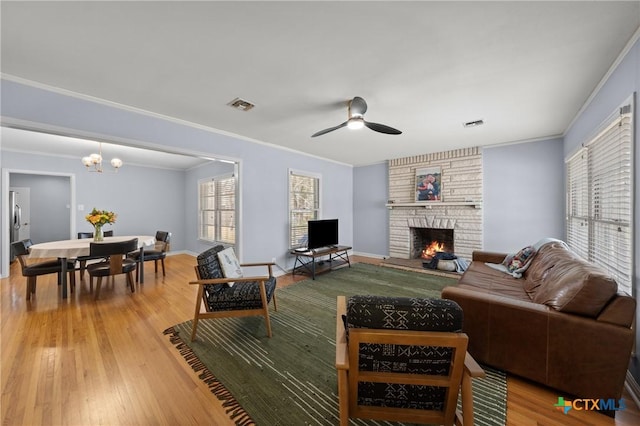 living area with a stone fireplace, visible vents, baseboards, ornamental molding, and light wood-type flooring