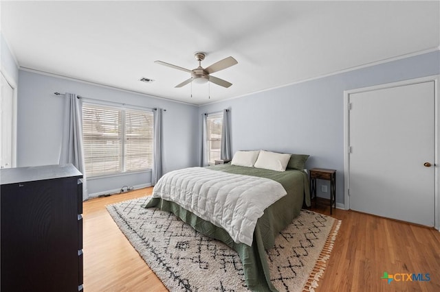 bedroom featuring ornamental molding, light wood-type flooring, visible vents, and a ceiling fan