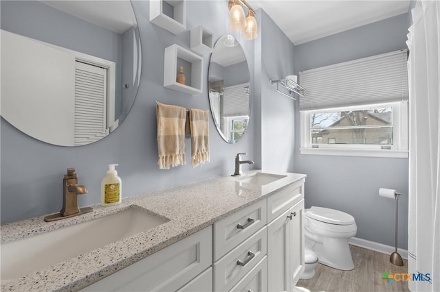 bathroom with baseboards, a sink, toilet, and double vanity