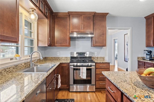 kitchen with light stone counters, under cabinet range hood, stainless steel appliances, a sink, and light wood-type flooring