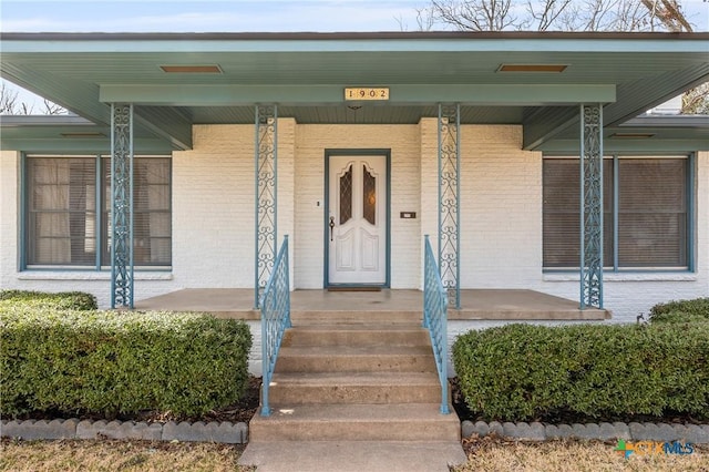 entrance to property featuring covered porch and brick siding