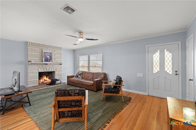 living area featuring crown molding, a fireplace, visible vents, and light wood-style floors