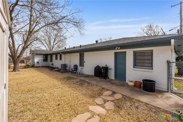 rear view of property featuring a lawn, a patio, fence, central AC, and brick siding