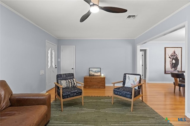 living area featuring light wood-style floors, baseboards, visible vents, and crown molding