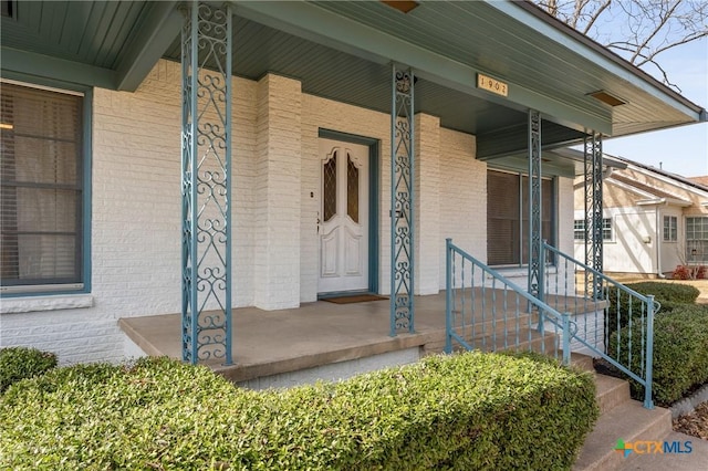 doorway to property with a porch and brick siding