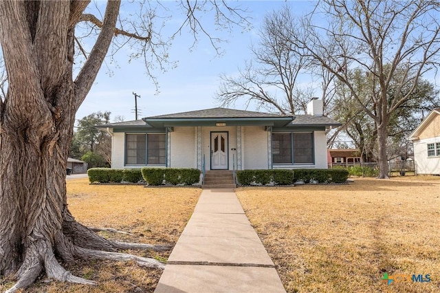 bungalow-style home featuring brick siding, a chimney, a porch, a front yard, and fence