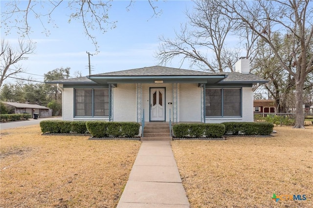 bungalow featuring covered porch, brick siding, fence, a front lawn, and a chimney