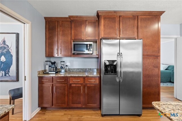 kitchen with stainless steel appliances, light wood-type flooring, baseboards, and light stone countertops