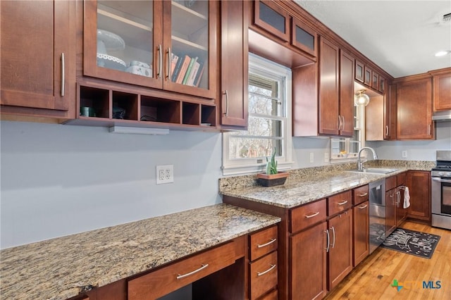 kitchen with glass insert cabinets, light stone counters, stainless steel appliances, light wood-style floors, and a sink