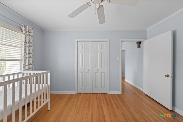 unfurnished bedroom featuring crown molding, a closet, light wood-style floors, ceiling fan, and baseboards