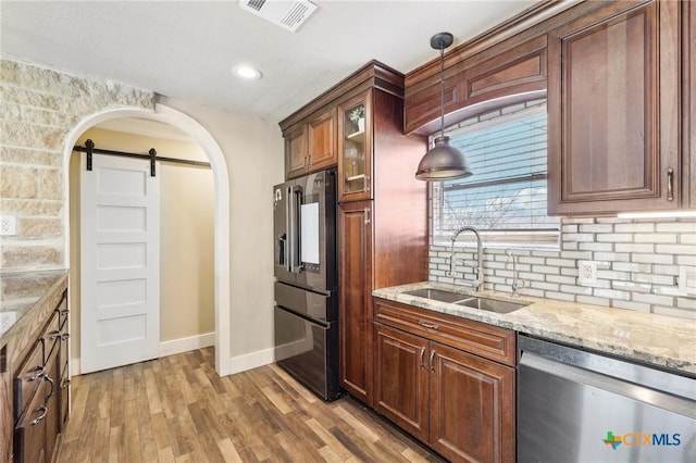 kitchen featuring high end fridge, sink, stainless steel dishwasher, pendant lighting, and a barn door