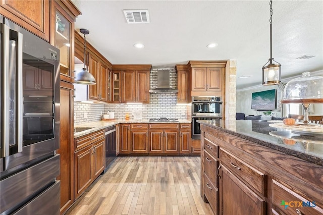 kitchen featuring wall chimney range hood, appliances with stainless steel finishes, hanging light fixtures, decorative backsplash, and dark stone counters