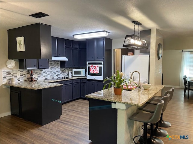 326 Riverview Rd, Mcqueeney, TX 78123 - kitchen with white appliances, a peninsula, a kitchen bar, tasteful backsplash, and under cabinet range hood