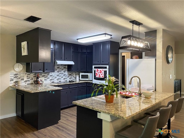 326 Riverview Rd, Mcqueeney, TX 78123 - kitchen featuring white appliances, dark wood finished floors, light stone countertops, a peninsula, and a textured ceiling