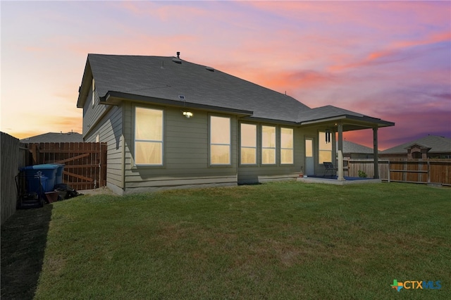 back house at dusk with a patio and a lawn