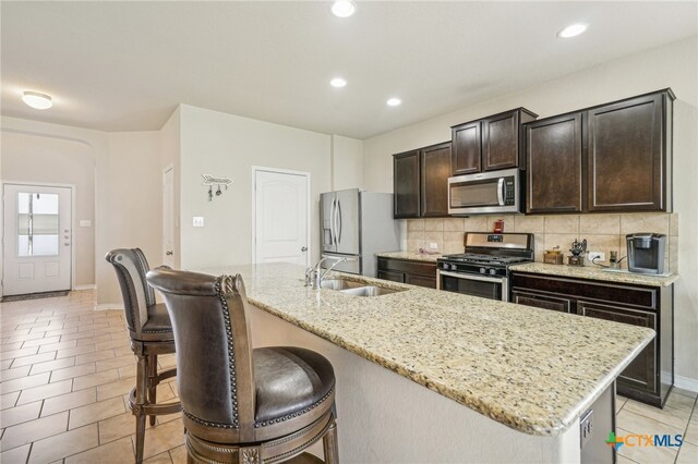 kitchen with appliances with stainless steel finishes, decorative backsplash, sink, a breakfast bar, and a kitchen island with sink