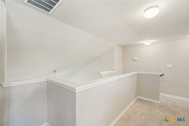 hallway with vaulted ceiling, light colored carpet, and a textured ceiling