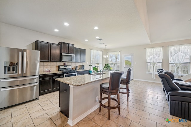 kitchen with a kitchen bar, stainless steel appliances, sink, tasteful backsplash, and an island with sink