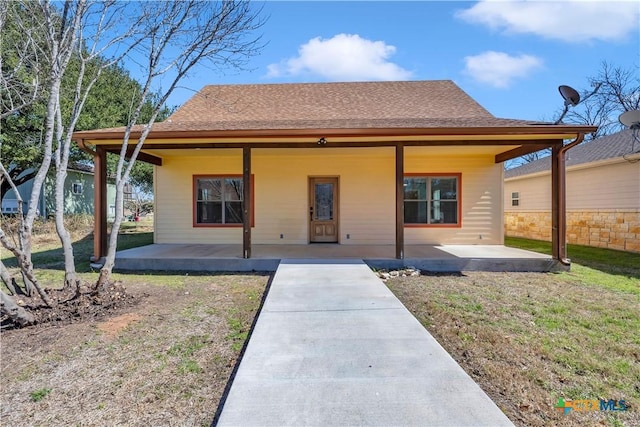 view of front facade featuring roof with shingles, a patio, and a front lawn