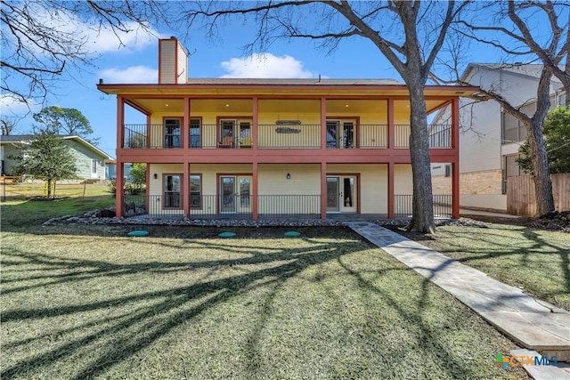 back of house with a balcony, fence, a yard, french doors, and a chimney