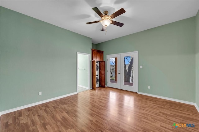 unfurnished room featuring stacked washer and dryer, baseboards, wood finished floors, and french doors