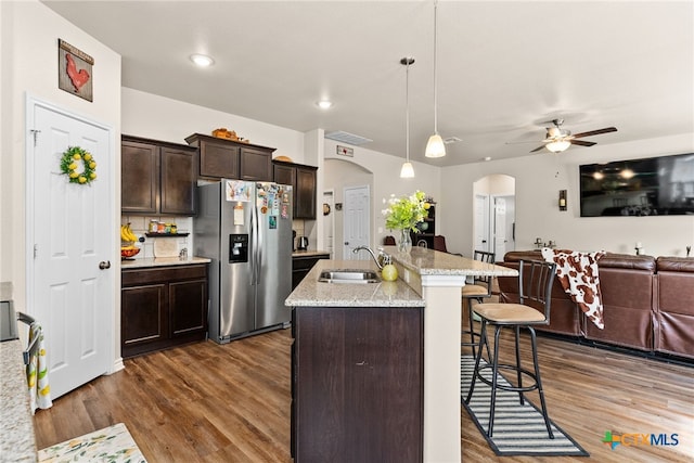 kitchen with dark wood-type flooring, sink, an island with sink, stainless steel fridge with ice dispenser, and pendant lighting