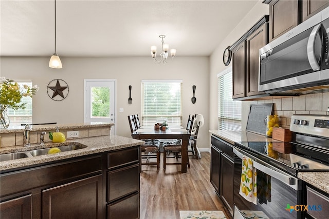 kitchen featuring light wood-type flooring, appliances with stainless steel finishes, dark brown cabinetry, pendant lighting, and sink