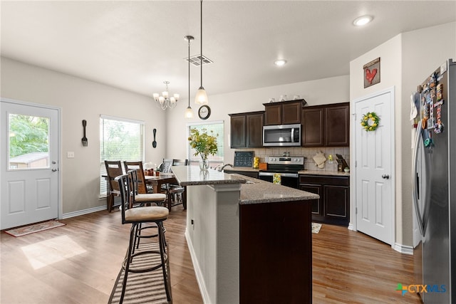 kitchen featuring a center island with sink, stainless steel appliances, dark brown cabinetry, light stone countertops, and light hardwood / wood-style floors