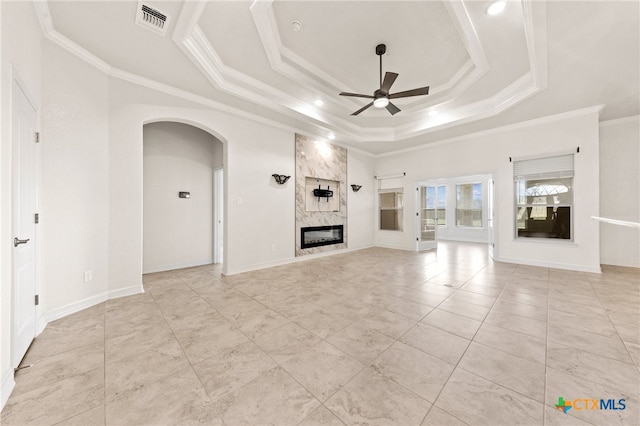 unfurnished living room with a high end fireplace, a tray ceiling, ceiling fan, and ornamental molding