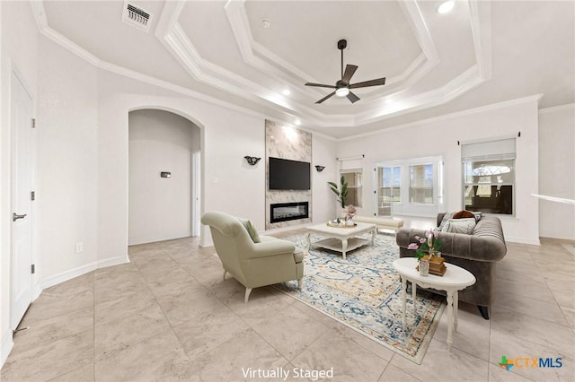 tiled living room with a raised ceiling, ceiling fan, crown molding, and a high end fireplace