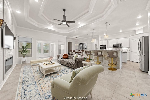 living room featuring ceiling fan, a raised ceiling, light tile patterned floors, and crown molding