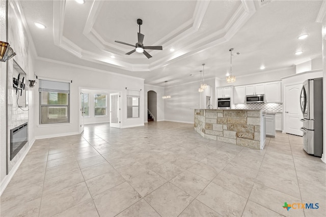 tiled living room featuring ceiling fan, a stone fireplace, ornamental molding, and a tray ceiling