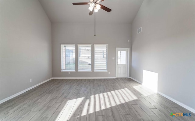 empty room with ceiling fan, light hardwood / wood-style flooring, and a towering ceiling